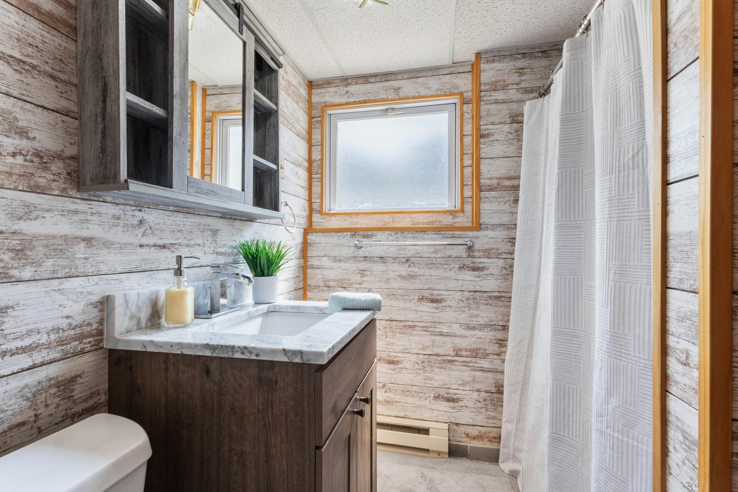 Bright modern bathroom with rustic wood accents, featuring a marble countertop sink and shower.